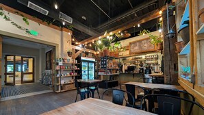 A cafe with wooden tables and chairs, a refrigerated display case, and hanging plants.
