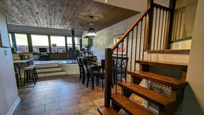 A spacious kitchen with a dining area, a wooden staircase, and a view of the outdoors.