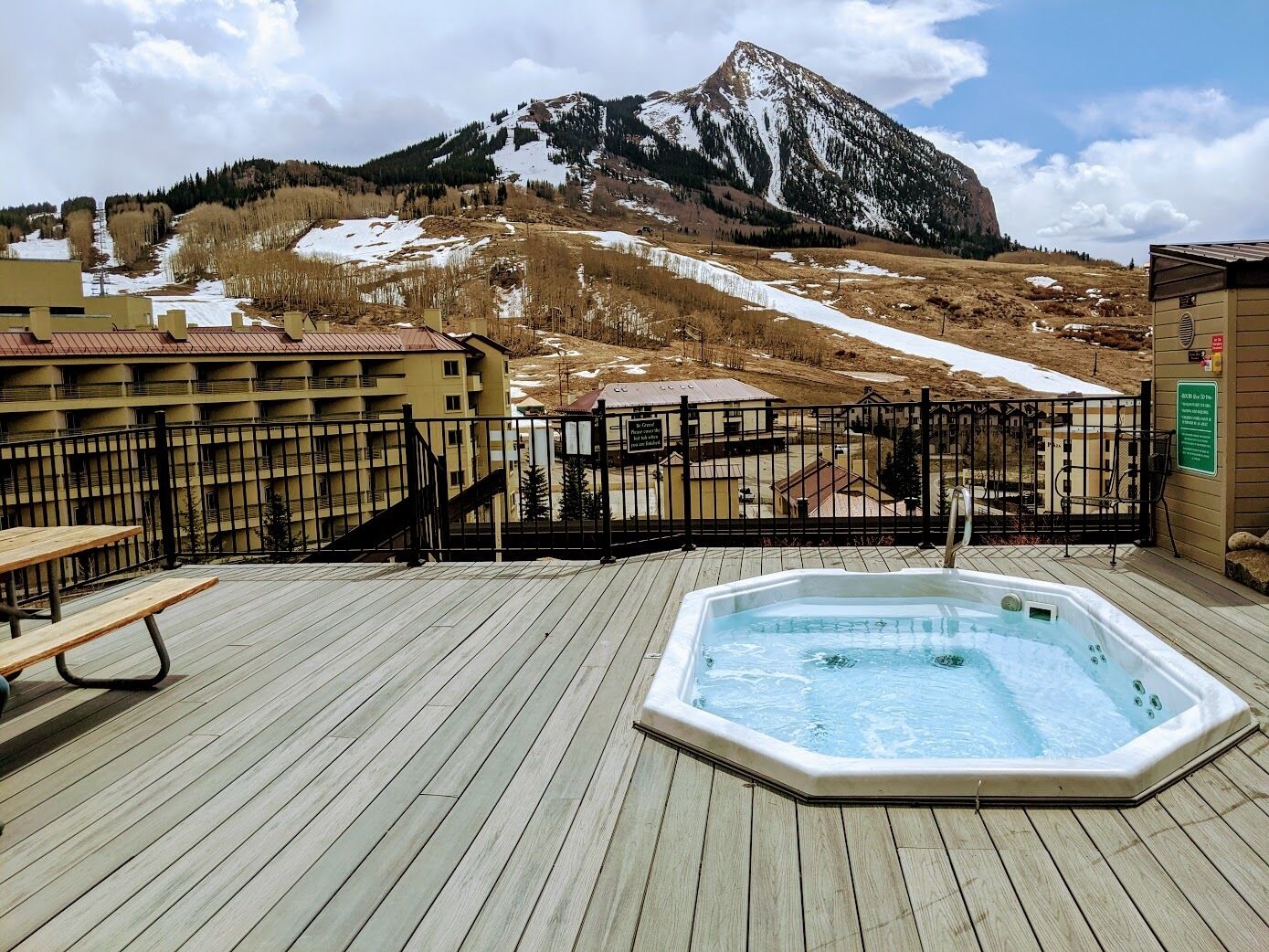 Um deck de madeira com hidromassagem, mesa de piquenique e vista para as montanhas.