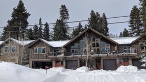A large, multi-story wooden house with a garage, surrounded by snow and tall evergreen trees. - Luxury 2 Bedroom, 2 Bath Condo - Perfect for a Fun Filled Family Get Away! (Mammoth Lakes)
