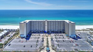 Un grand hôtel à étages, doté d’une tour centrale, situé près d’une plage et disposant d’un parking en face.