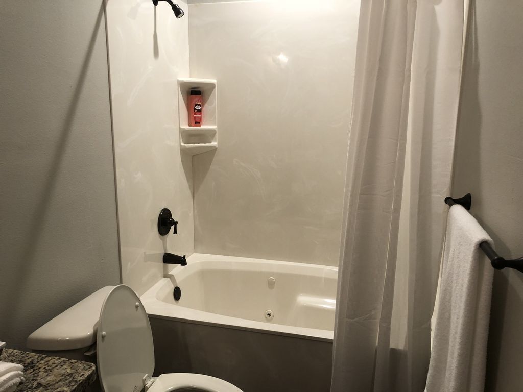 Un baño con bañera, inodoro y un estante con artículos de aseo.