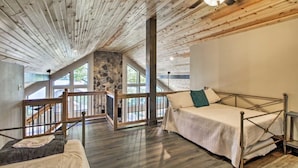 Une chambre avec un plafond en pente, un mur en pierre, un lit et une vue sur l’extérieur.