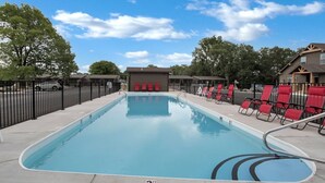 Une piscine rectangulaire dont la profondeur est indiquée par un repère à 3 pieds, entourée de chaises longues rouges et d’une clôture noire.