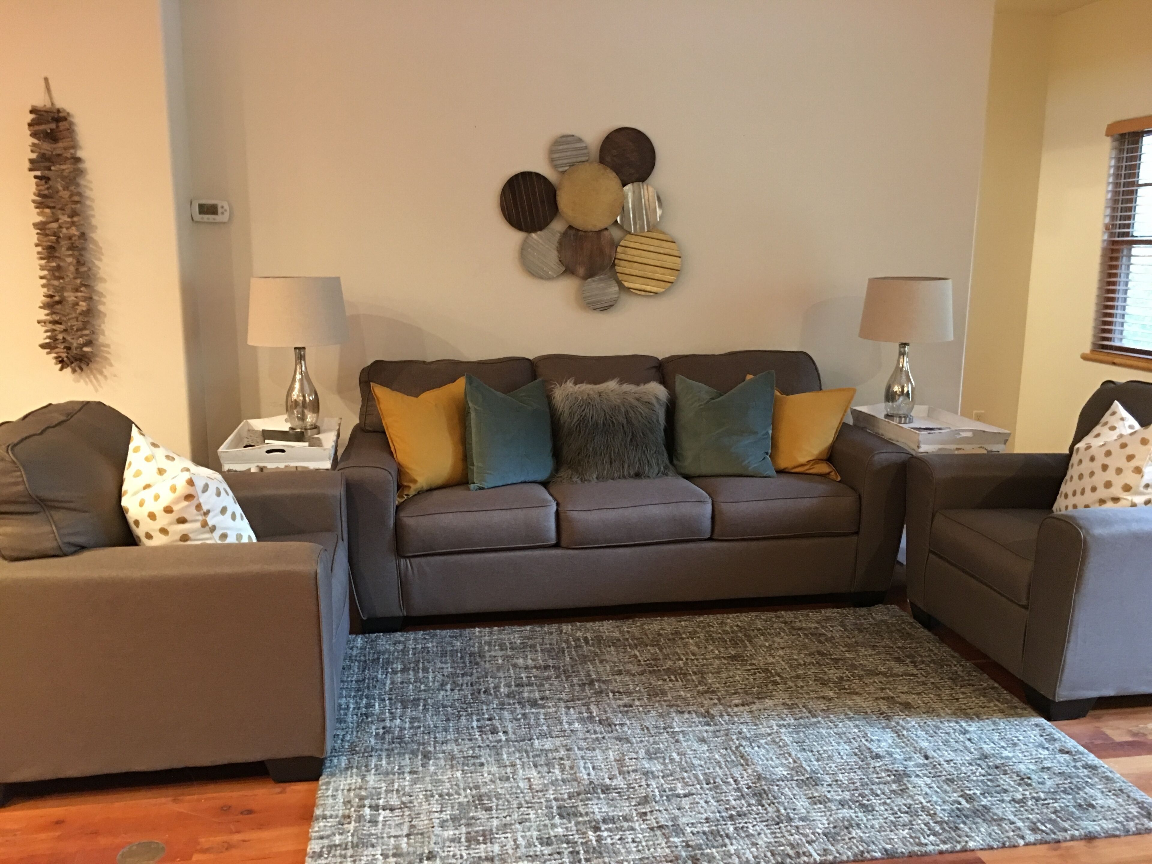 Un salon avec un canapé gris, un tapis à motifs et des éléments de décoration murale.