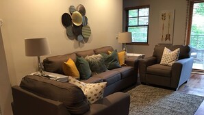 A living room with a brown sectional sofa, two armchairs, a coffee table, a lamp, and a decorative wall piece. - This beautiful, spacious condo is located right off Main Street in Ouray. (Ouray)