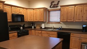 A kitchen with wooden cabinets, a black refrigerator, a stove, a sink, and a window with blinds. - This beautiful, spacious condo is located right off Main Street in Ouray. (Ouray)