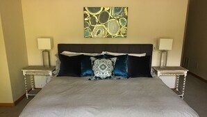 A neatly made bed with striped bedding, two bedside tables with lamps, and a decorative wall piece above the bed. - This beautiful, spacious condo is located right off Main Street in Ouray. (Ouray)