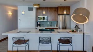 A modern kitchen with white countertops, wooden cabinets, and a central island with bar stools.