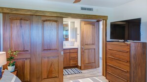 A room with wooden wardrobes, a television, and a ceiling fan.