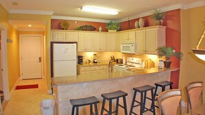 A kitchen with a central island, bar stools, a refrigerator, a stove, and various kitchen appliances. - LUXURIOUS CONDO ON THE BEACH includes FREE BEACH CHAIRS. (Panama City Beach)