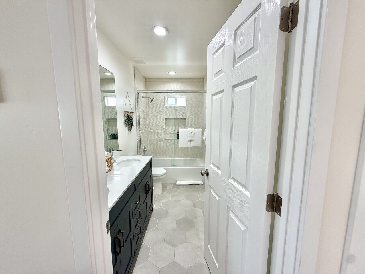 A modern bathroom with a white vanity, a glass shower enclosure, and a hexagonal tile floor.
