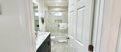 Een moderne badkamer met een witte wastafel, een douchecabine van glas en een vloer van honingraatmozaïek.
