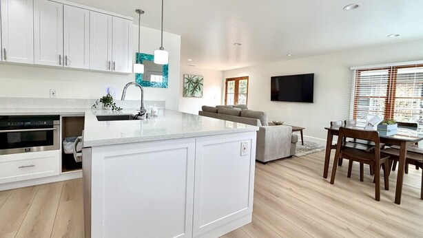 A modern kitchen with white cabinetry, a central island, and a dining area with wooden chairs and a table. - JULY 2026 NEW REMODEL... Mermaid`s Cove, Nestled between Beach and Bay! (San Diego)