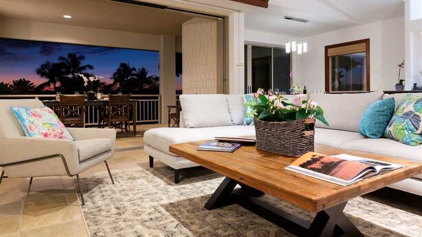A modern living room with a sofa, coffee table, and a view of palm trees at dusk.
