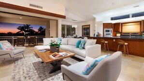 A modern living room with a sofa, armchairs, and a coffee table. There is a kitchen area with a bar and a dining area with chairs.