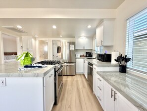 A modern kitchen with white cabinetry, stainless steel appliances, and a marble countertop.