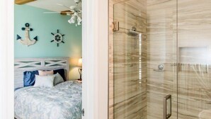 A bathroom with a glass shower enclosure, a bathtub, and a visible door leading to a bedroom with a bed and a nightstand. - Doc's Holiday updated 2bed/2bath half duplex with Cabana Club (Key Colony Beach)