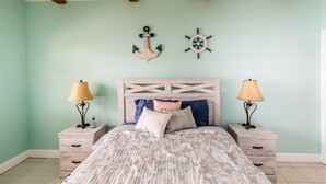 A bedroom with a bed, two nightstands, a wooden headboard, and two wall decorations. - Doc's Holiday updated 2bed/2bath half duplex with Cabana Club (Key Colony Beach)