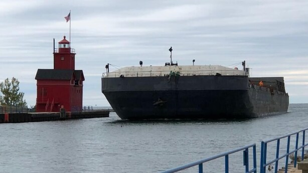Un gran carguero amarrado en el muelle, con un faro rojo al fondo.