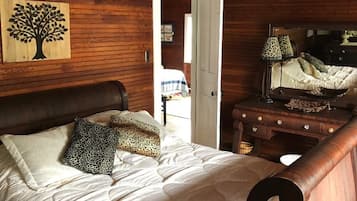 A wooden-paneled bedroom with a bed, a nightstand, a lamp, and a door leading to another room.