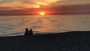Atardecer sobre un mar tranquilo con dos personas sentadas en la playa.