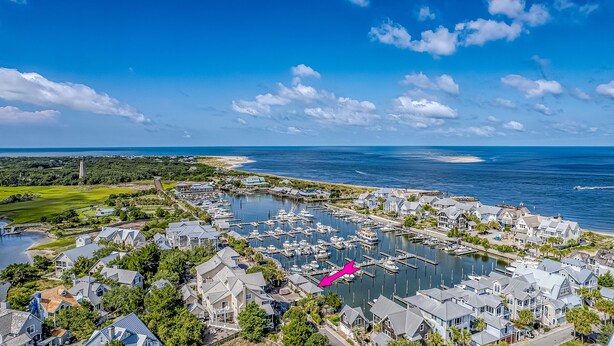 A coastal marina with multiple boats docked, surrounded by residential buildings and a clear view of the ocean. - Marina view one bedroom cottage close to amenities on BHI. Walking distance to the NC lighthouse (Bald Head Island)