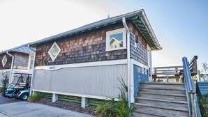 A wooden cabin with a 'WATER' sign, a small porch, and a golf cart parked outside. - Marina view one bedroom cottage close to amenities on BHI. Walking distance to the NC lighthouse (Bald Head Island)