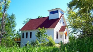 Una casa bianca con tetto rosso, circondata da erba alta e alberi.
