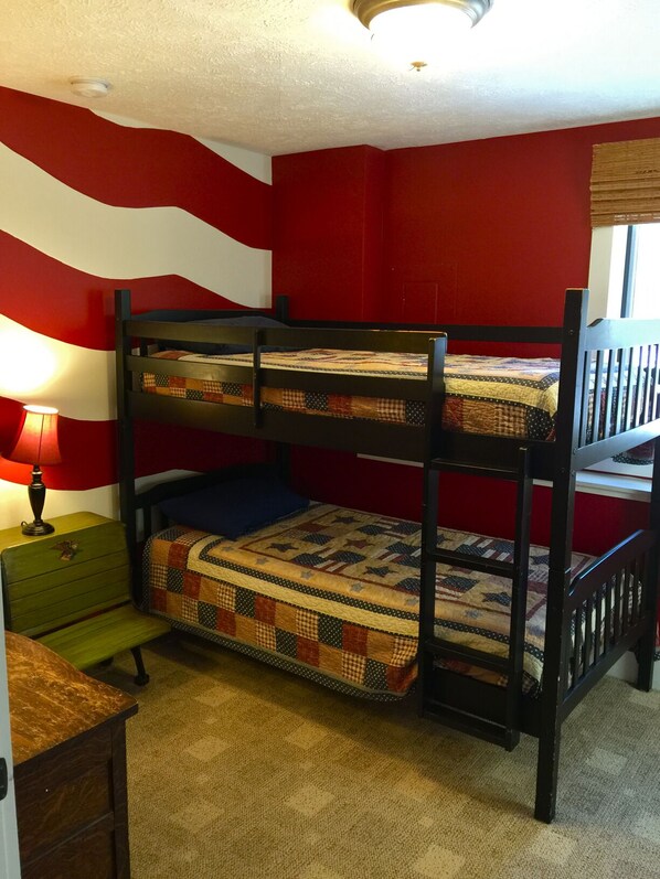 A bunk bed with a quilted mattress, a small bedside table with a lamp, and a green chair.
