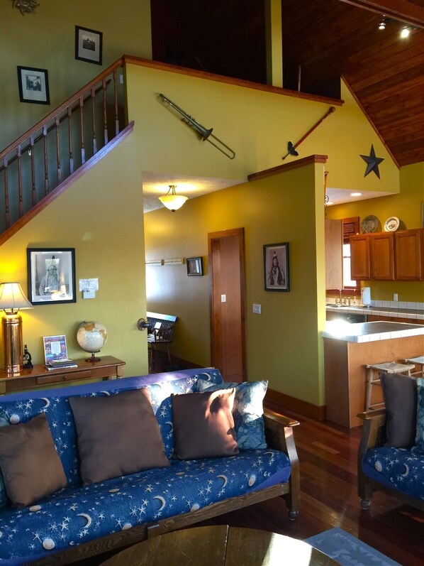 Una sala de estar acogedora con un sofá azul, una escalera de madera y una zona de cocina con armarios de madera.