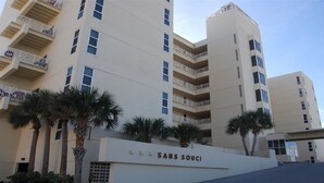 A multi-story hotel with balconies, palm trees, and a sign reading "SANS SOUCI". - Directly on the Gulf, larger end unit,  both bedrooms have water view! (Pensacola Beach)