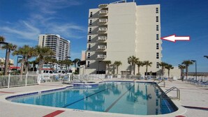 A swimming pool with a white fence and palm trees. There is a tall building with balconies in the background. - Directly on the Gulf, larger end unit,  both bedrooms have water view! (Pensacola Beach)