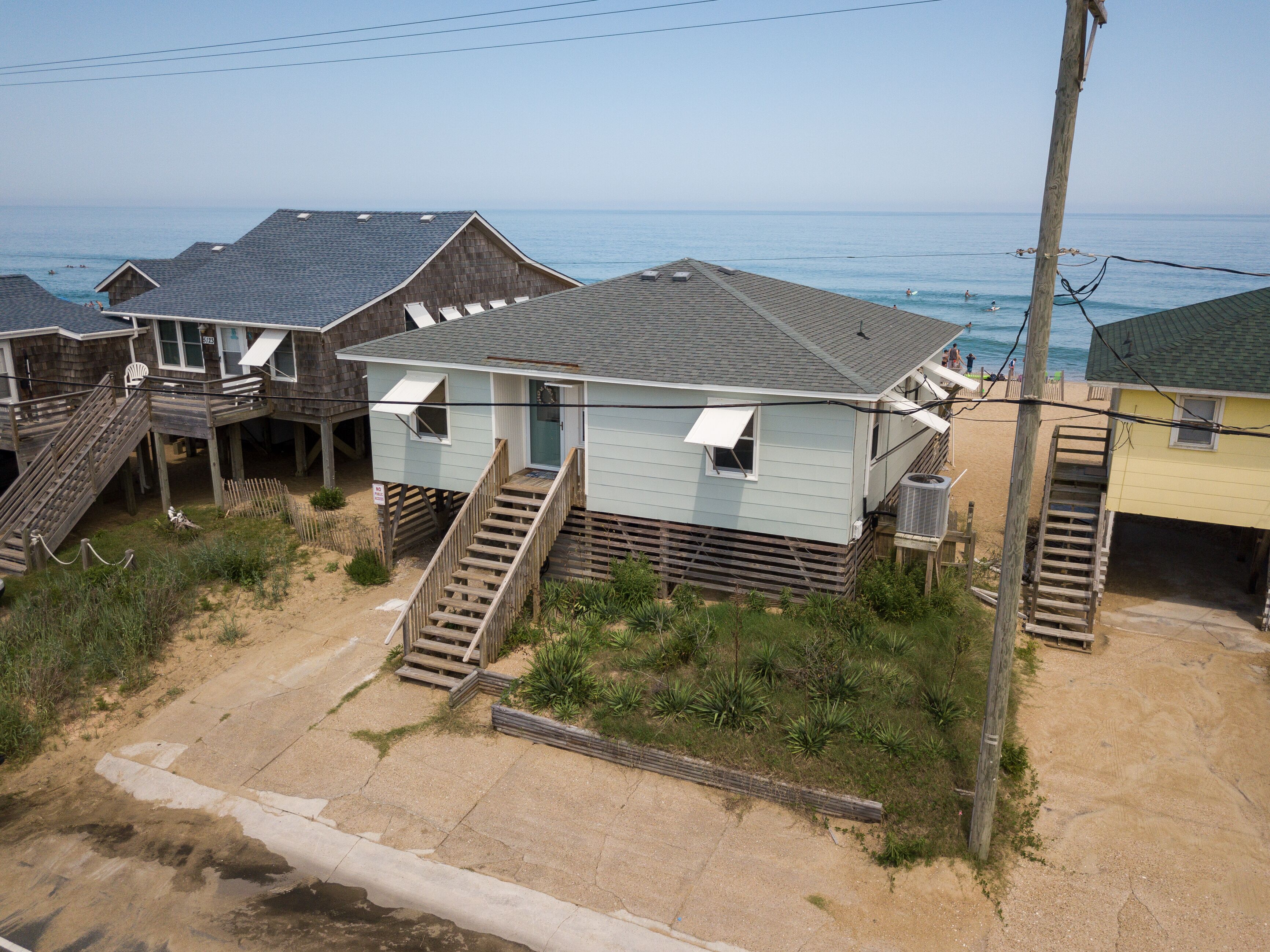 Een huis aan het strand met een houten terras, een trap naar een overdekte veranda en uitzicht op de oceaan.