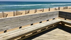 Un paseo marítimo de madera que conduce a una playa de arena, con el océano al fondo.