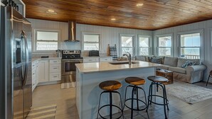 Una cocina moderna con techo de madera, armarios blancos y una isla central con taburetes.