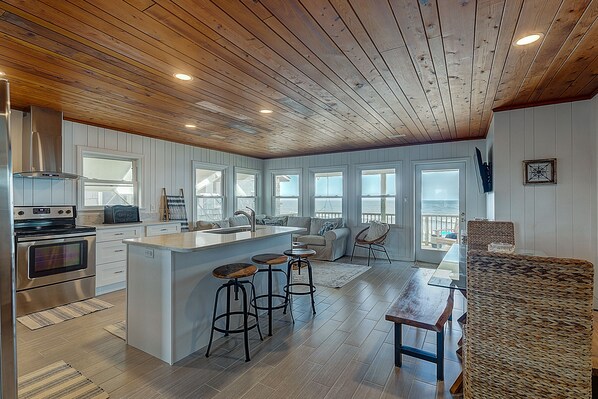 A spacious kitchen with wooden ceiling, a large island with stools, and a view to the outside.