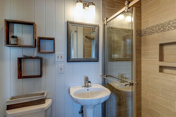 Une salle de bain avec un lavabo blanc, un miroir et une cabine de douche en verre.