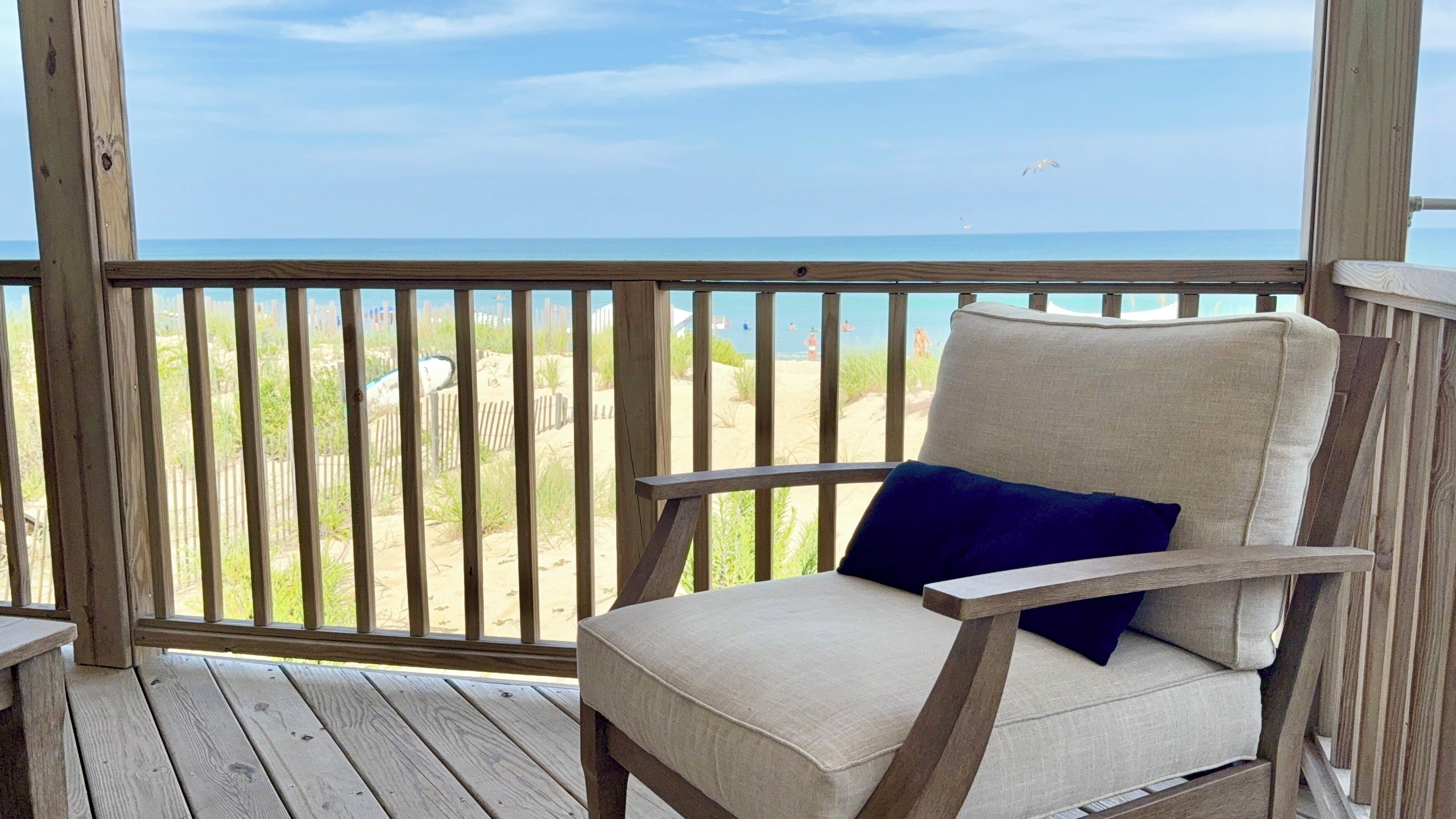 A wooden deck with a chair and a view of the beach.
