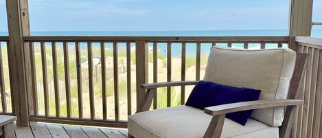 A wooden deck with a chair and a view of the beach.