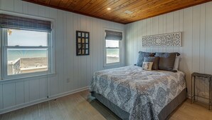Un dormitorio con una cama grande, techo de madera y dos ventanas vistas al mar.
