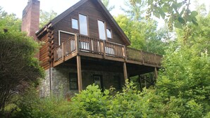 Een vakantiehuisje van hout met een stenen fundering, een houten balkon en een schoorsteen.