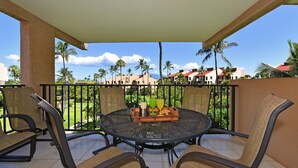 A balcony with a round table and four chairs, overlooking a green lawn and buildings. - Kam Sands -Innercourt- Ocean views- large lanai & very private third floor end  (Kihei)