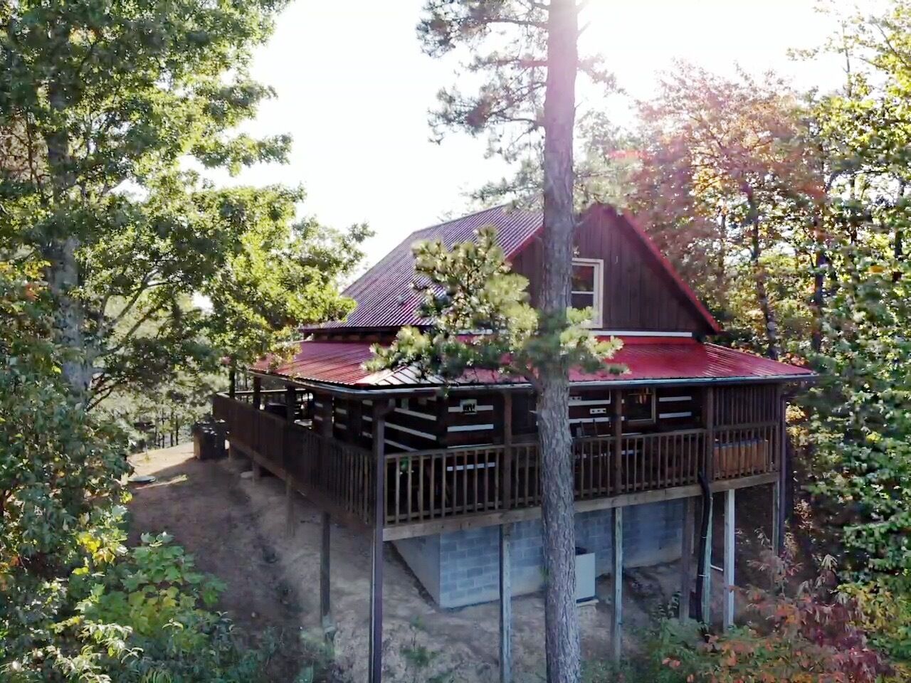 A cabin with a red roof, wooden deck, and a small porch.