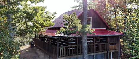 A cabin with a red roof, wooden deck, and a small porch.