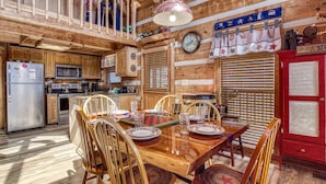 L’intérieur d’un chalet en bois comprend une table à manger pour quatre personnes, des appareils de cuisine et un buffet rouge.