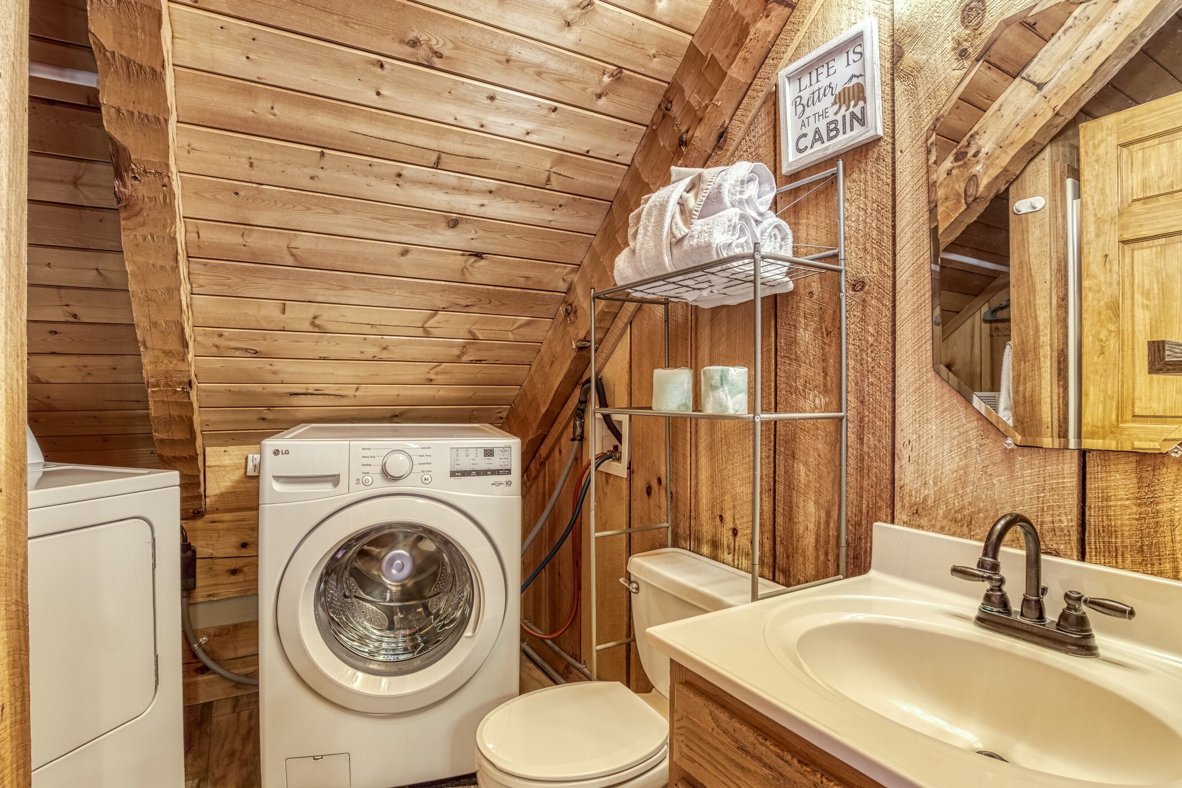 Ein kleines Badezimmer mit Holzwänden, einer Waschmaschine, einer Toilette und einem Waschbecken mit Spiegel.