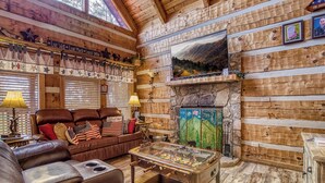 Un intérieur chaleureux de chalet en bois, avec un canapé en cuir, une table de baby-foot et une cheminée en pierre.