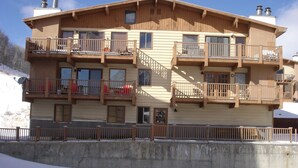 Un immeuble en bois à plusieurs étages, doté de balcons, d’un mur de soutènement en béton et d’un sol enneigé.