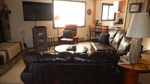 Un salon avec un canapé en cuir marron, un téléviseur, une table à manger avec des chaises et une lampe.